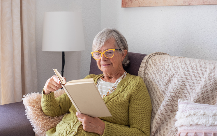 Senior Retired Woman with Eyeglasses Relaxing on Home Sofa Reading a Book. Serene Retirement Lifestyle Senior Retired Woman with Eyeglasses Relaxing on Home Sofa Reading a Book. Serene Retirement Lifestyle