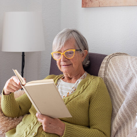 Senior Retired Woman with Eyeglasses Relaxing on Home Sofa Reading a Book. Serene Retirement Lifestyle Senior Retired Woman with Eyeglasses Relaxing on Home Sofa Reading a Book. Serene Retirement Lifestyle